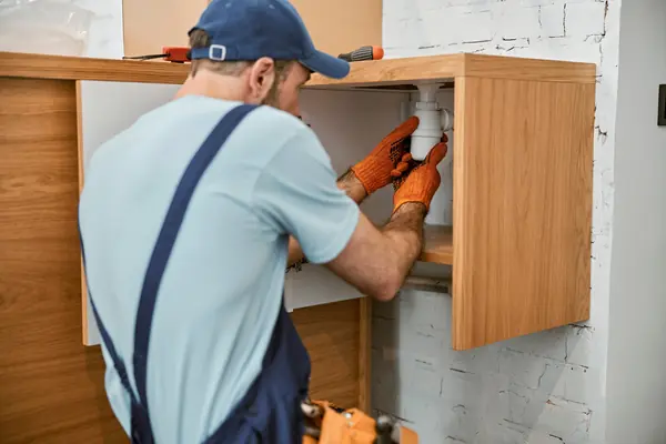 4 male-plumber-in-cap-repairing-pipe-in-kitchen-2022-09-22-18-32-34-utc